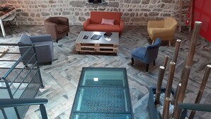 Une pièce avec un mur en pierre, une table basse en bois, une table en verre et différents types de sièges, notamment un canapé et des fauteuils.