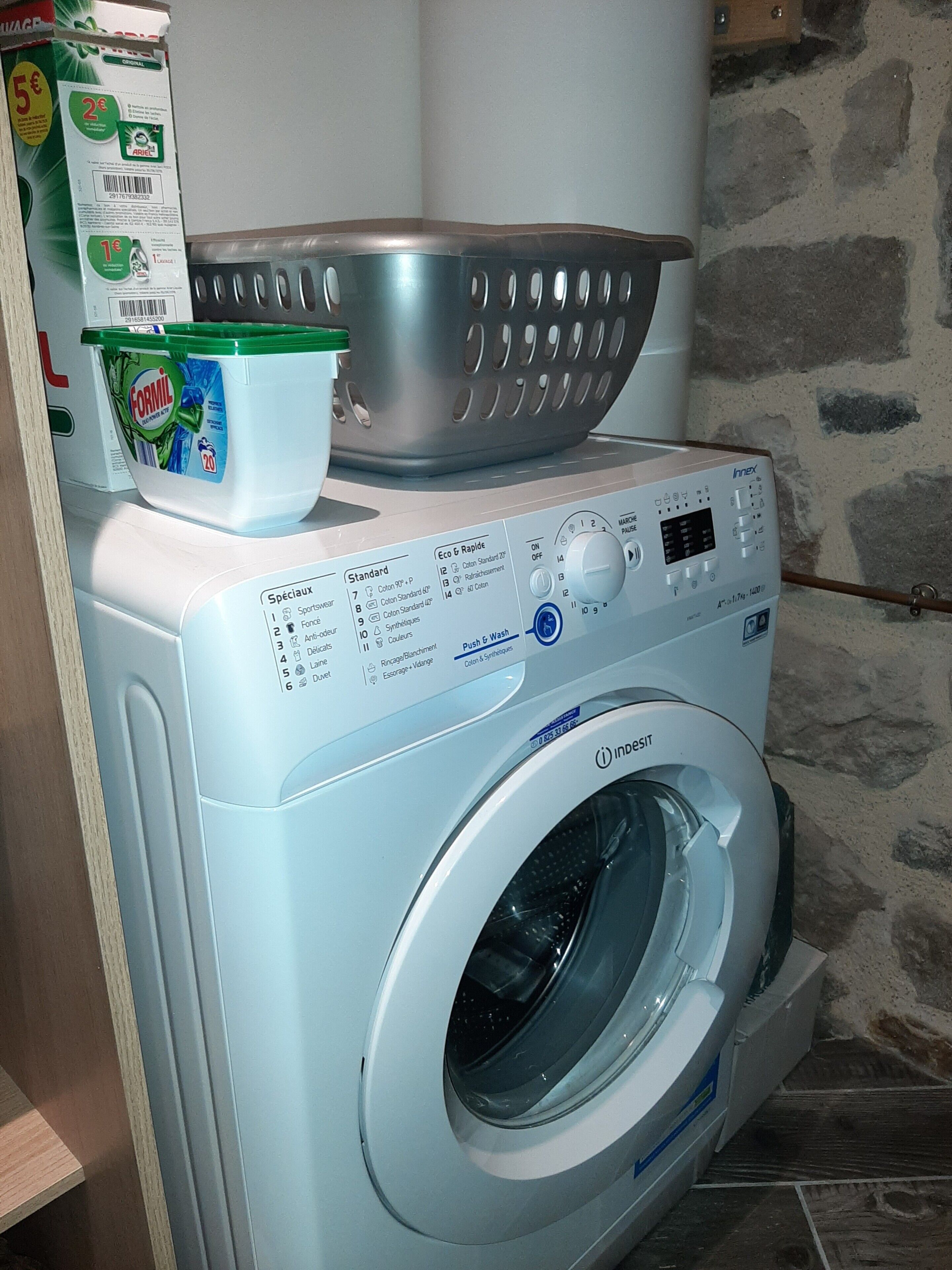 Une machine à laver à chargement frontal, dotée d’un panneau de commande, d’un compartiment à lessive et d’un panier en métal situé sur le dessus.