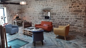 Une pièce aux murs de pierre, avec un canapé, des fauteuils, une table et un bureau doté d’une lampe.