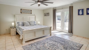 A bedroom with a bed, a ceiling fan, a nightstand, a window with curtains, and a door leading outside. - Backyard Oasis & Hot Tub: Mtn-view Wickenburg Home (Wickenburg)