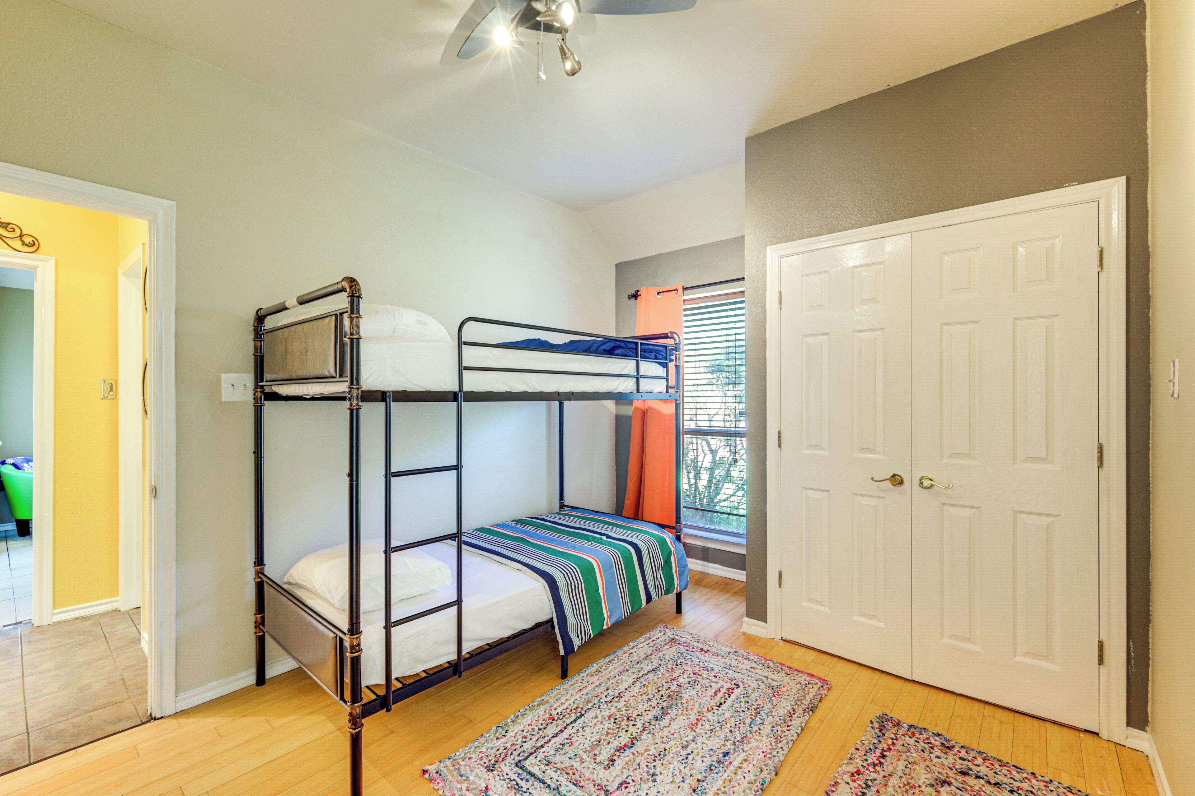 Une chambre avec un lit superposé, un ventilateur de plafond, une porte et une fenêtre avec des stores.