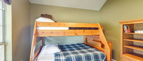 A bunk bed with a plaid bedspread and pillows, a wooden dresser with open shelves, and a ceiling fan with lights.