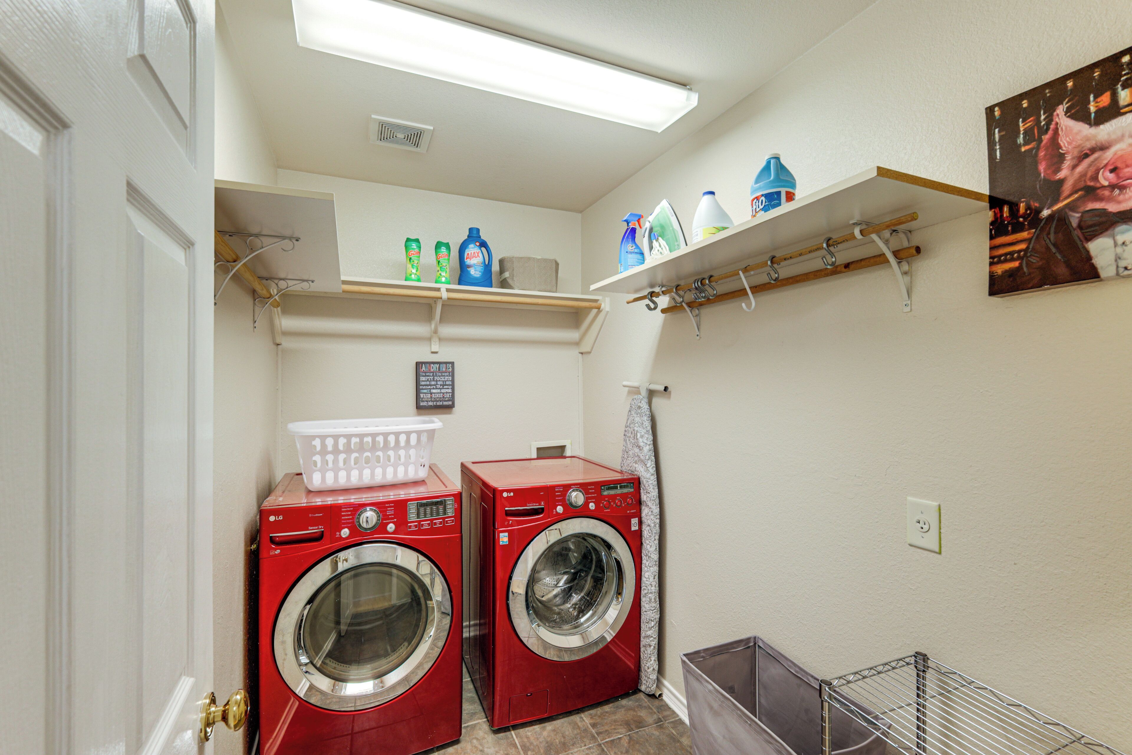 A laundry room with two red front-loading washers, shelves with laundry supplies, and a metal rack.
