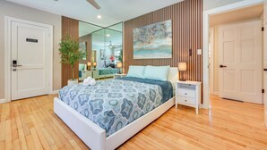 Une chambre moderne avec un grand lit, un ventilateur de plafond, une table de chevet avec une lampe, un miroir et une porte portant l’inscription « Chambre d’amis ».