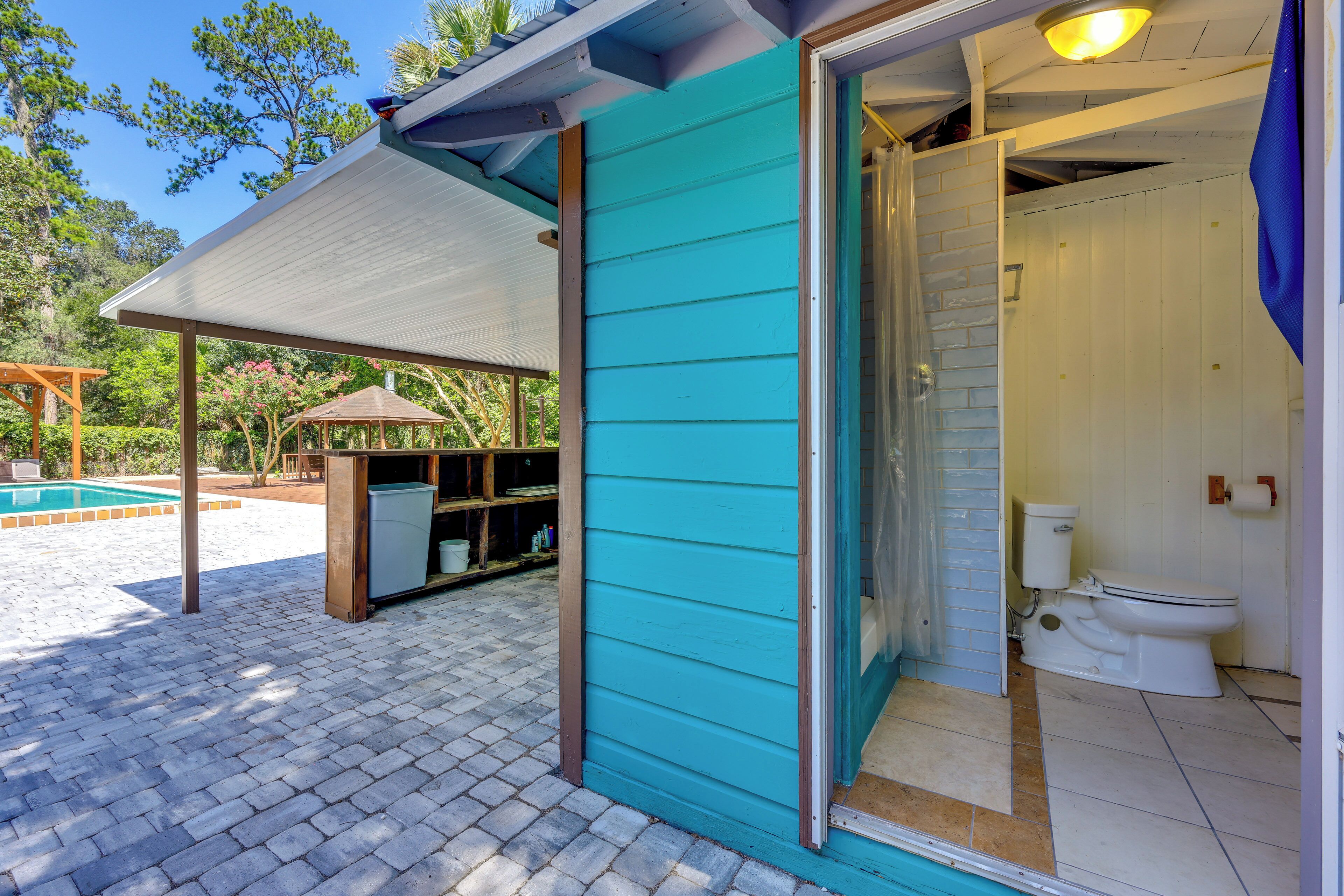 A turquoise building with a covered patio, a pool, and a bathroom with a toilet and shower.