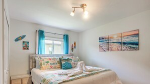 A bedroom with a bed, a nightstand, a window with curtains, and a beach-themed wall art.