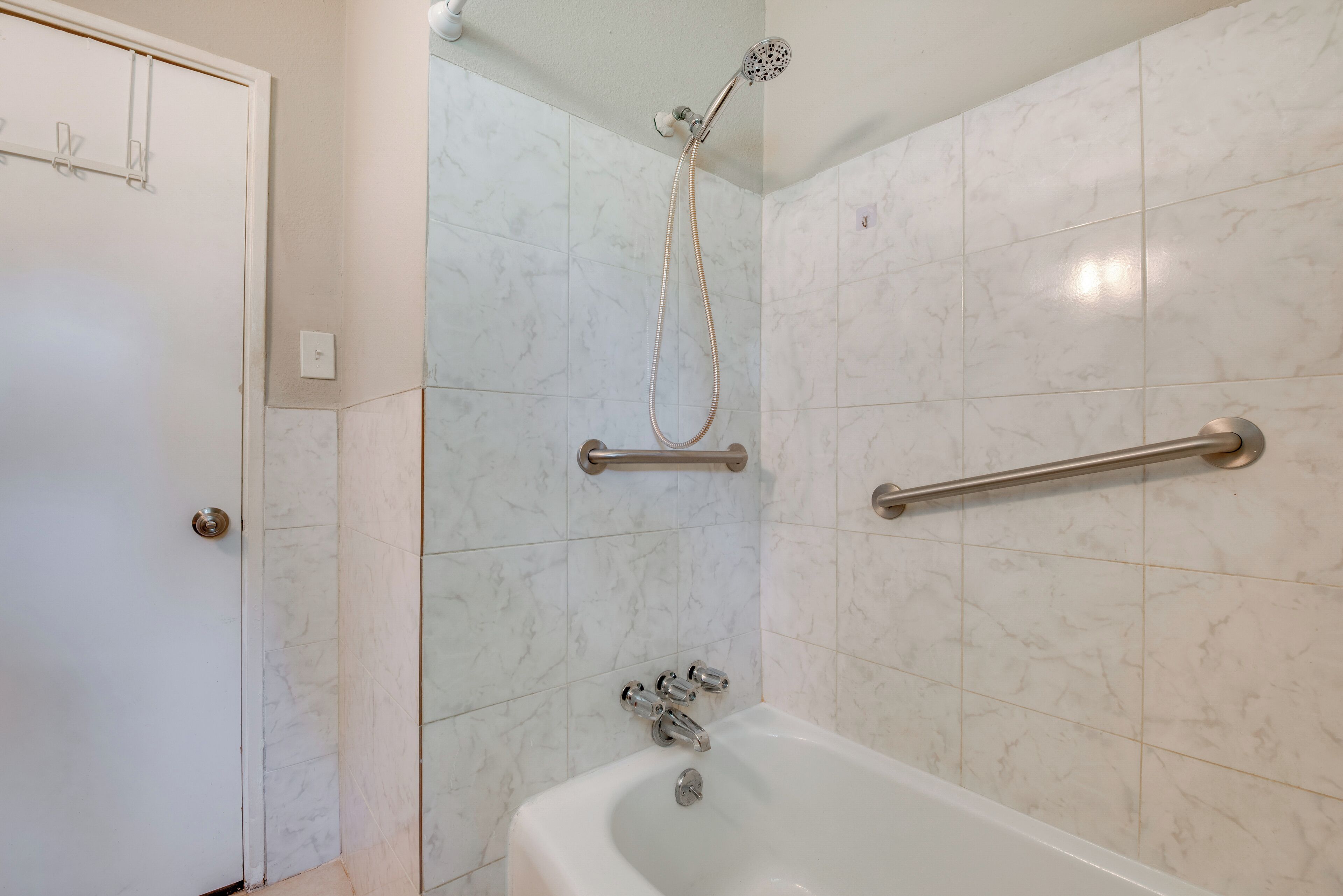 A bathroom with a bathtub, a showerhead, and a handrail.