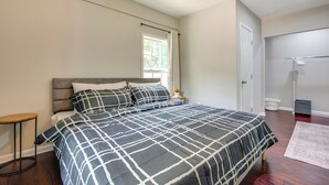 A bedroom with a large bed, a small round table, a ceiling fan, a window with curtains, and a door leading to another room. - Inviting Home w/ Backyard: 8 Mi to Dtwn Atlanta! (Atlanta)