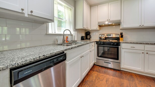 A modern kitchen with white cabinets, a granite countertop, a dishwasher, an oven, and a window with curtains. - Inviting Home w/ Backyard: 8 Mi to Dtwn Atlanta! (Atlanta)