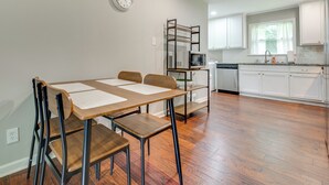 A modern kitchen with white cabinets, a microwave, and a dishwasher. There is a dining table with chairs and a clock on the wall. - Inviting Home w/ Backyard: 8 Mi to Dtwn Atlanta! (Atlanta)