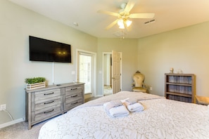 A bedroom with a large bed, a ceiling fan, a dresser, a television, and a wooden cabinet.
