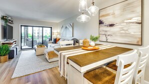 A modern living room with a wooden dining table, white chairs, and a large abstract painting.