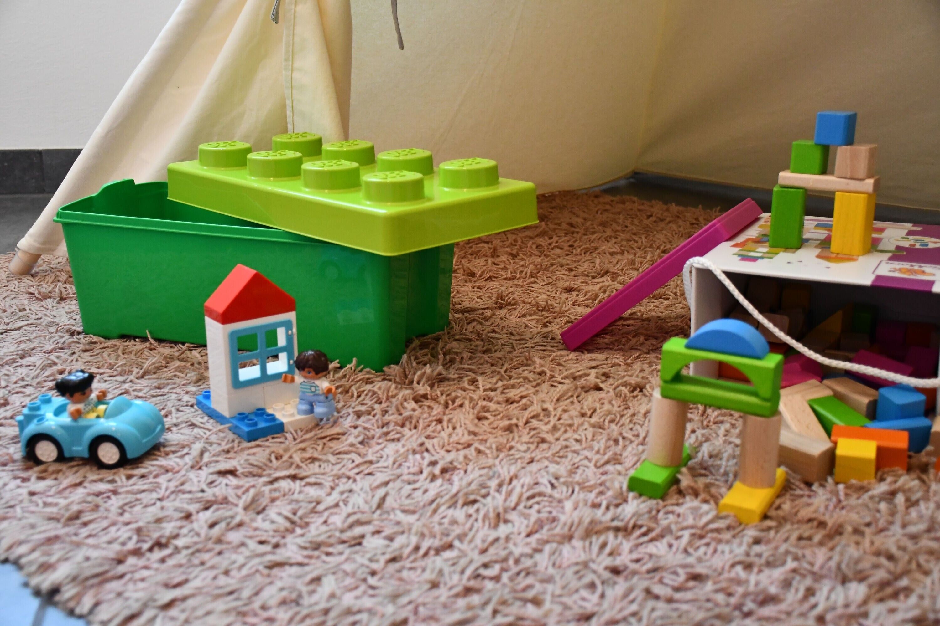 A play area with a green bin, a small blue car, and a tent.