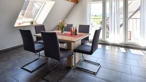 Zona pranzo con tavolo, sedie, un vaso con fiori e vista attraverso ampie finestre.