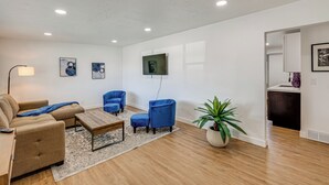 Un soggiorno moderno con un divano, due poltrone blu, un tavolino da caffè e una TV a parete.