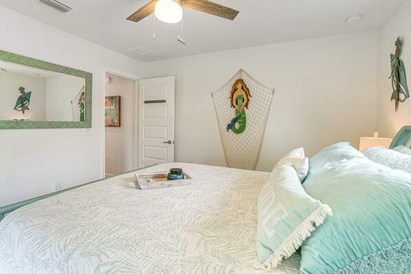 A bedroom with a bed, a ceiling fan, a door, and a wall decoration. - Golf Course-facing Poolside Oasis in Rotonda West! (Rotonda West)
