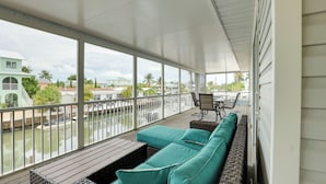 A covered outdoor area with a wooden deck, a teal sofa, and a table with chairs. - Canal-front Florida Keys Home w/ Private Dock (Marathon)