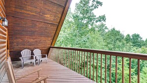 Een houten terras met Adirondack stoelen, een houten leuning en uitzicht op een dicht bos.