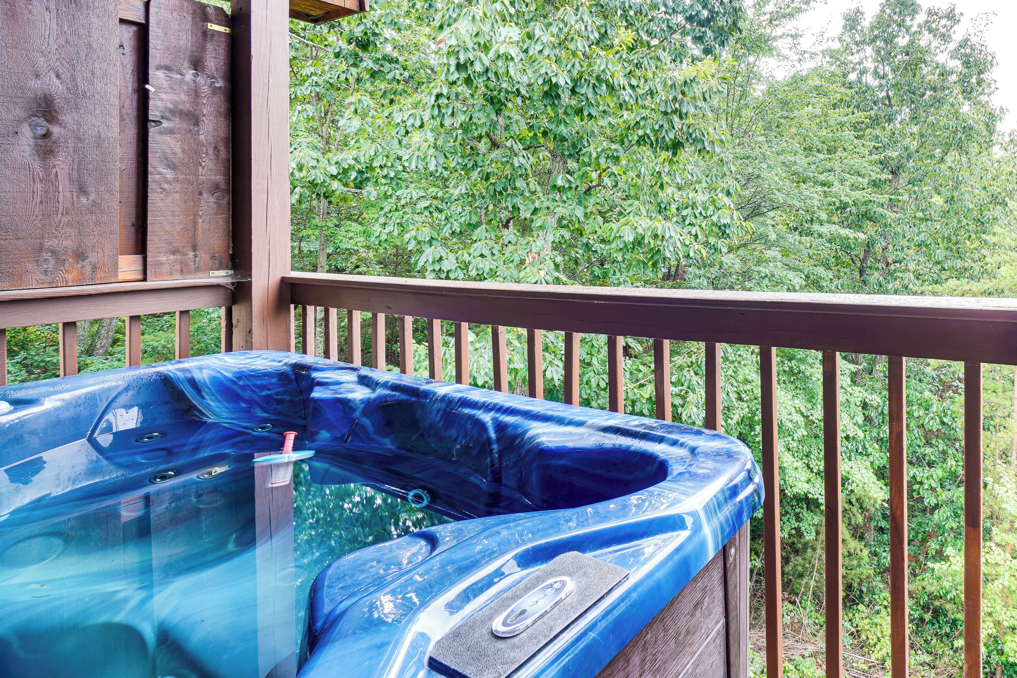 A hot tub on a wooden deck with a view of dense green foliage.