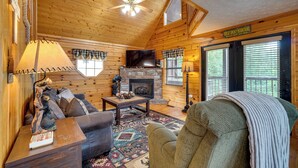 Een gezellig blokhutinterieur met een open haard, houten wanden, een plafondventilator en een bordje met de tekst 'Great Smoky Mountains'.