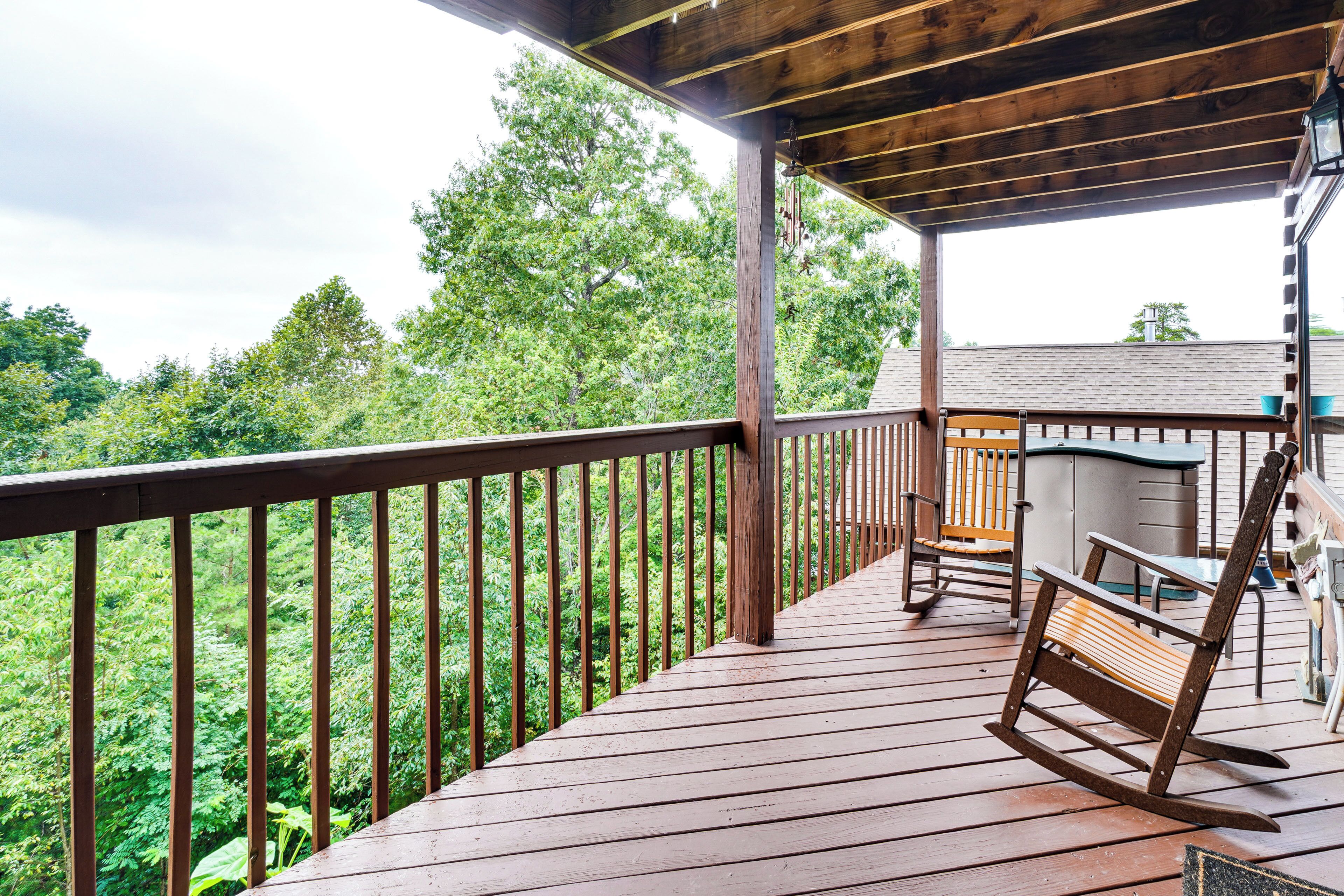 A wooden deck with a railing, a rocking chair, and a view of a forested area.