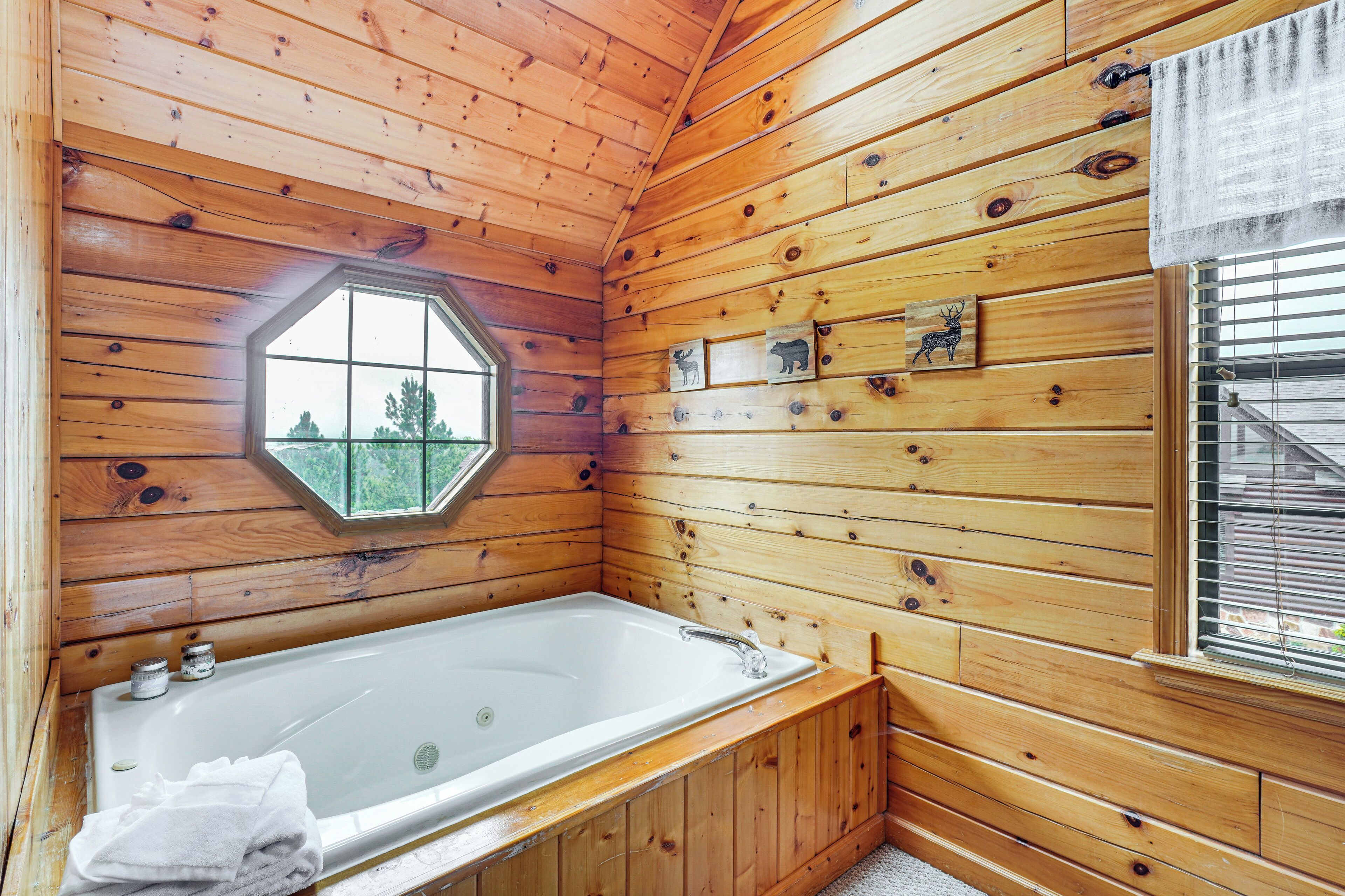Ein Badezimmer einer Holzhütte mit einer großen Badewanne, einem Dachfenster und einem Fenster mit Jalousien.