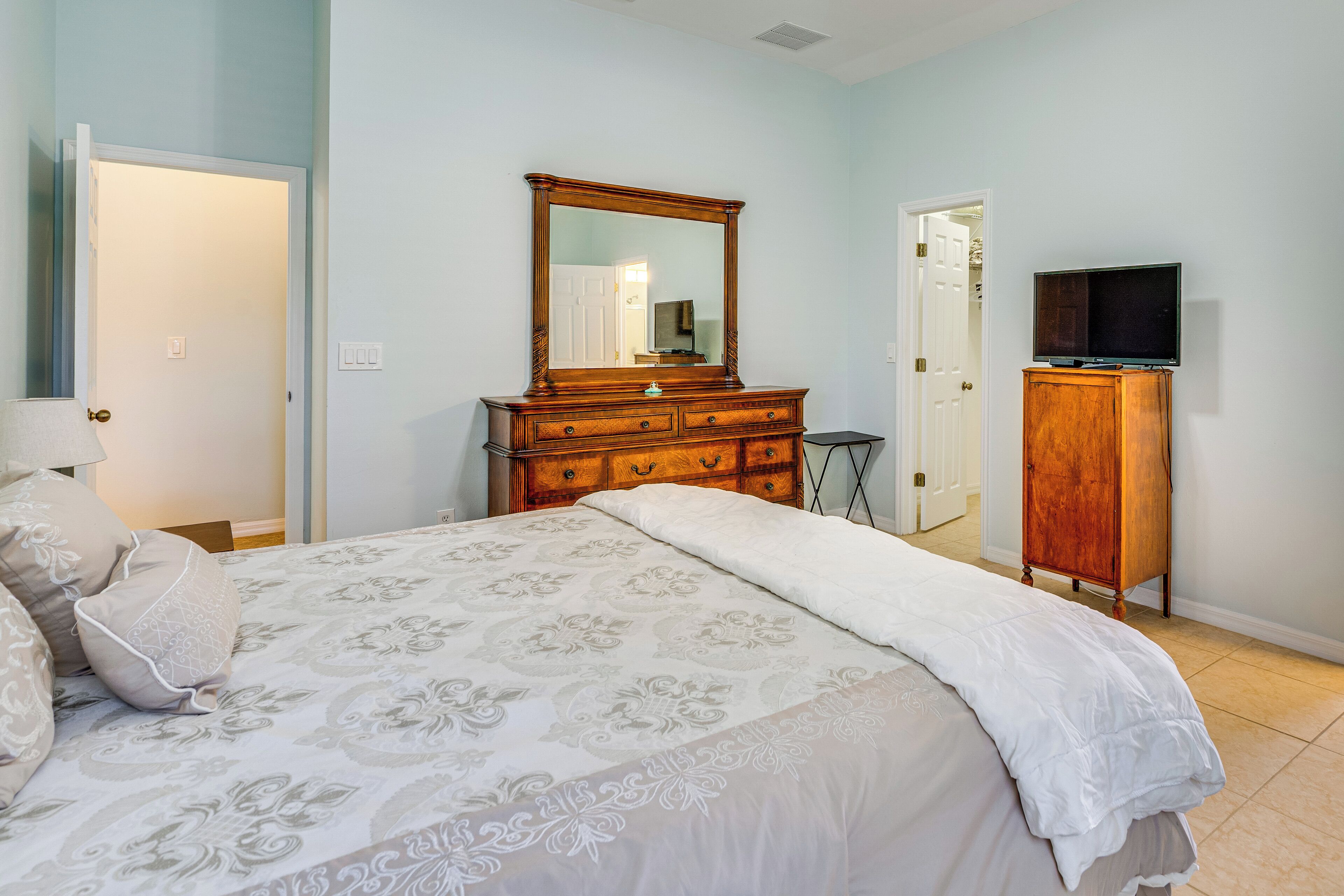 Un dormitorio con cama, cómoda, espejo y televisor.