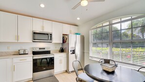 A modern kitchen with white cabinets, stainless steel appliances, and a dining area with a table and chairs. - 4 Mi to Beaches: Fort Myers Escape w/ Patio (Fort Myers)