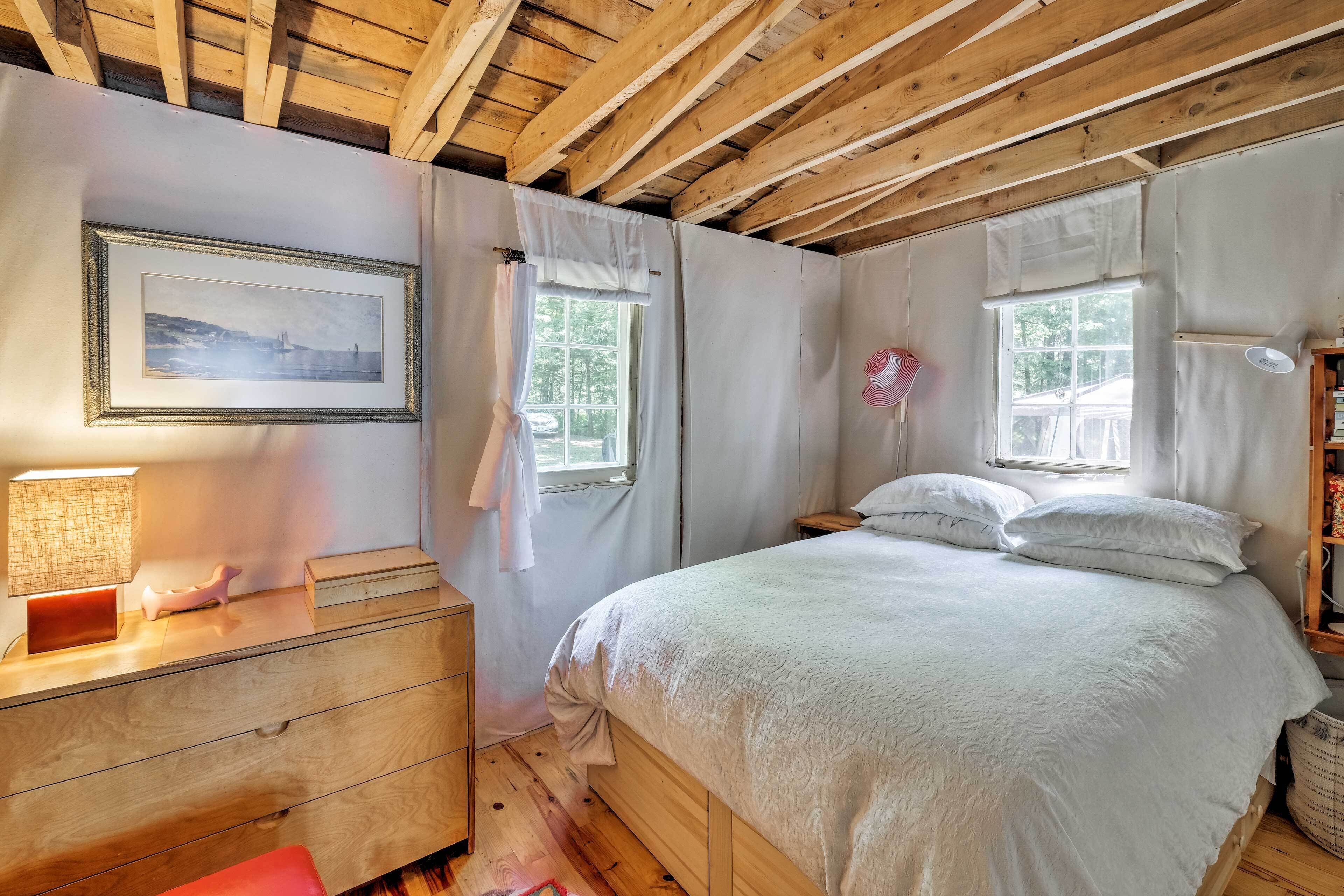 Une chambre avec un plafond en bois, un lit avec une literie blanche, une table de chevet avec une lampe et un tableau encadré au mur.