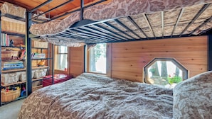 A cozy room with a bunk bed, a bookshelf filled with books and toys, and a window with a view of trees. - Cozy Lakefront Madison Cabin w/ Dock & Kayaks (Madison)