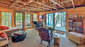 A spacious wooden cabin with a high ceiling, large windows, a cozy seating area, and a bookshelf. - Cozy Lakefront Madison Cabin w/ Dock & Kayaks (Madison)