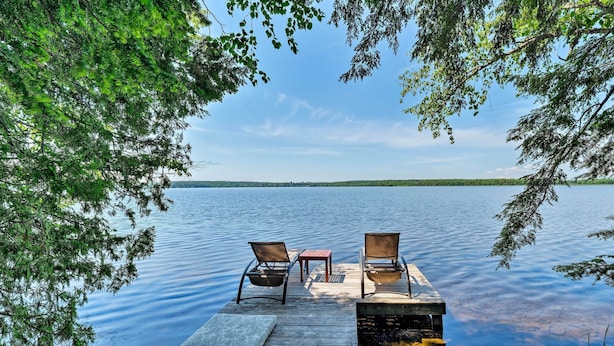 A wooden dock extending into a calm lake, with two chairs and a small table. - Cozy Lakefront Madison Cabin w/ Dock & Kayaks (Madison)