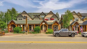 A row of multi-story buildings with a central entrance, a street in front, and a grey pickup truck parked on the side. - Patio w/ Peak 1 Mtn View: Main Street Frisco Condo (Frisco)