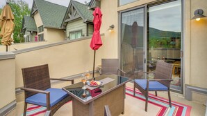 A balcony with wicker chairs, a glass table, and a red umbrella. - Patio w/ Peak 1 Mtn View: Main Street Frisco Condo (Frisco)