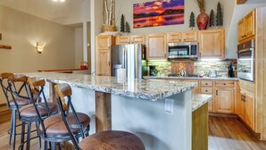 A kitchen with a large island, wooden cabinets, stainless steel appliances, and a decorative painting. - Patio w/ Peak 1 Mtn View: Main Street Frisco Condo (Frisco)