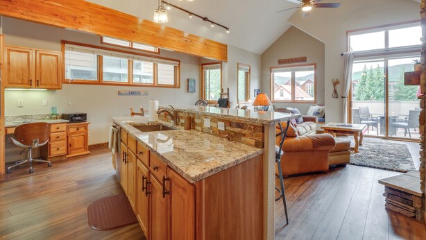 A spacious kitchen with wooden cabinets, a granite countertop, and a large island. There is a dining area with a leather couch and a stone fireplace. - Patio w/ Peak 1 Mtn View: Main Street Frisco Condo (Frisco)