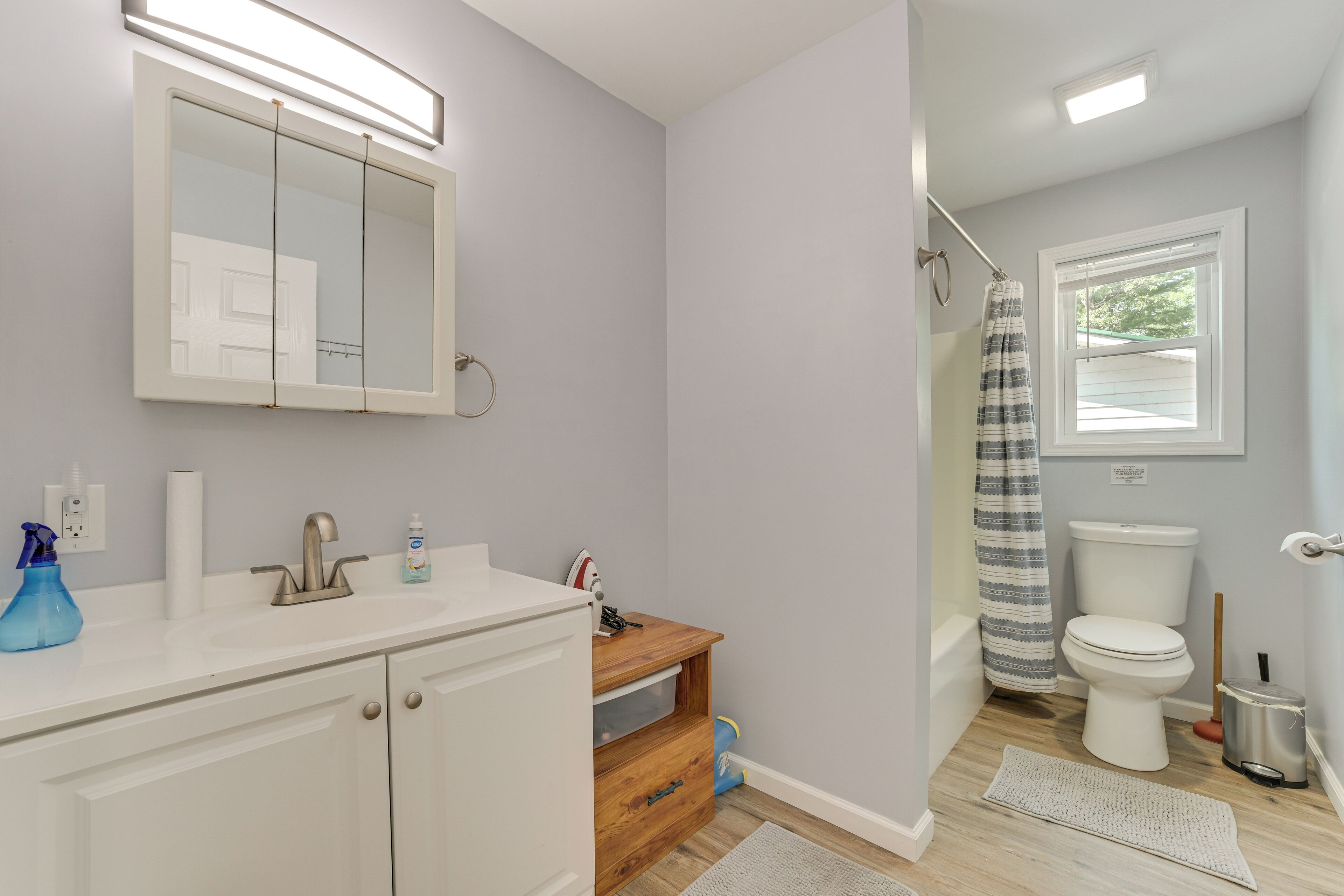 A bathroom with a white sink, mirror, and toilet, wooden vanity, and a shower curtain.