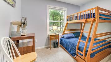 A bunk bed with a desk and chair, a standing fan, a window, and a trash can.