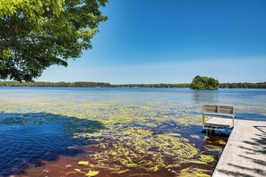 A wooden dock extending into a lake with clear water and floating vegetation. - Solberg Lake House: Dock, Deck + Stunning Views! (Phillips)