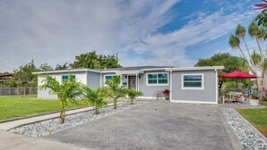 A two-story house with a paved driveway, a small patio area, and a red umbrella. - 2 Mi to Hard Rock Stadium: Home w/ Spacious Yard (Miami Gardens)