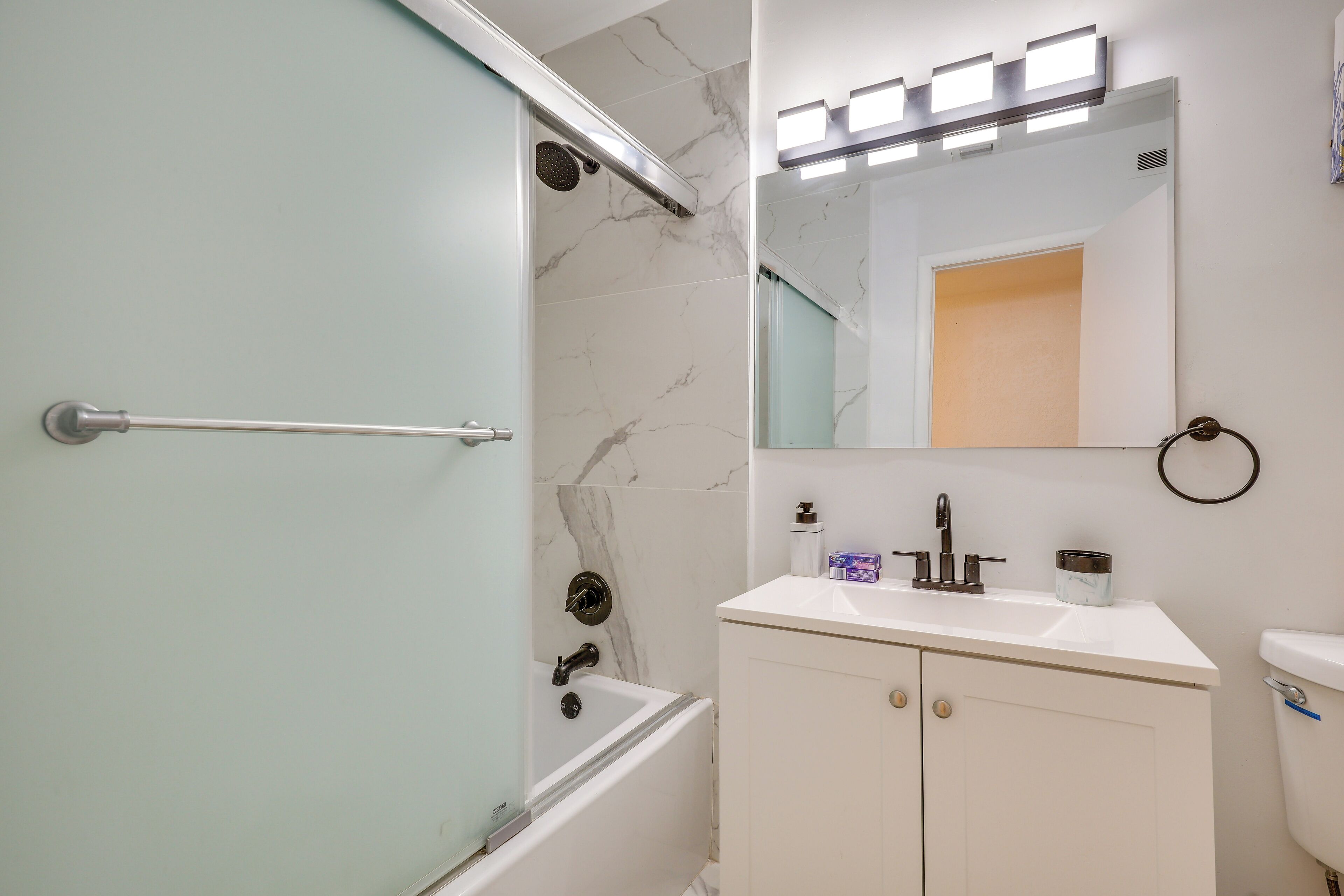 Un baño con puerta de ducha de vidrio, una bañera blanca, un tocador con espejo y un inodoro.
