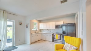 A modern kitchen with white cabinets, stainless steel appliances, and a yellow armchair. - 2 Mi to Hard Rock Stadium: Home w/ Spacious Yard (Miami Gardens)
