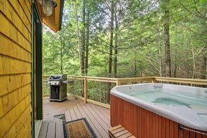 Eine Holzterrasse mit Whirlpool, Grill und Sitzgelegenheit, umgeben von einem Wald.