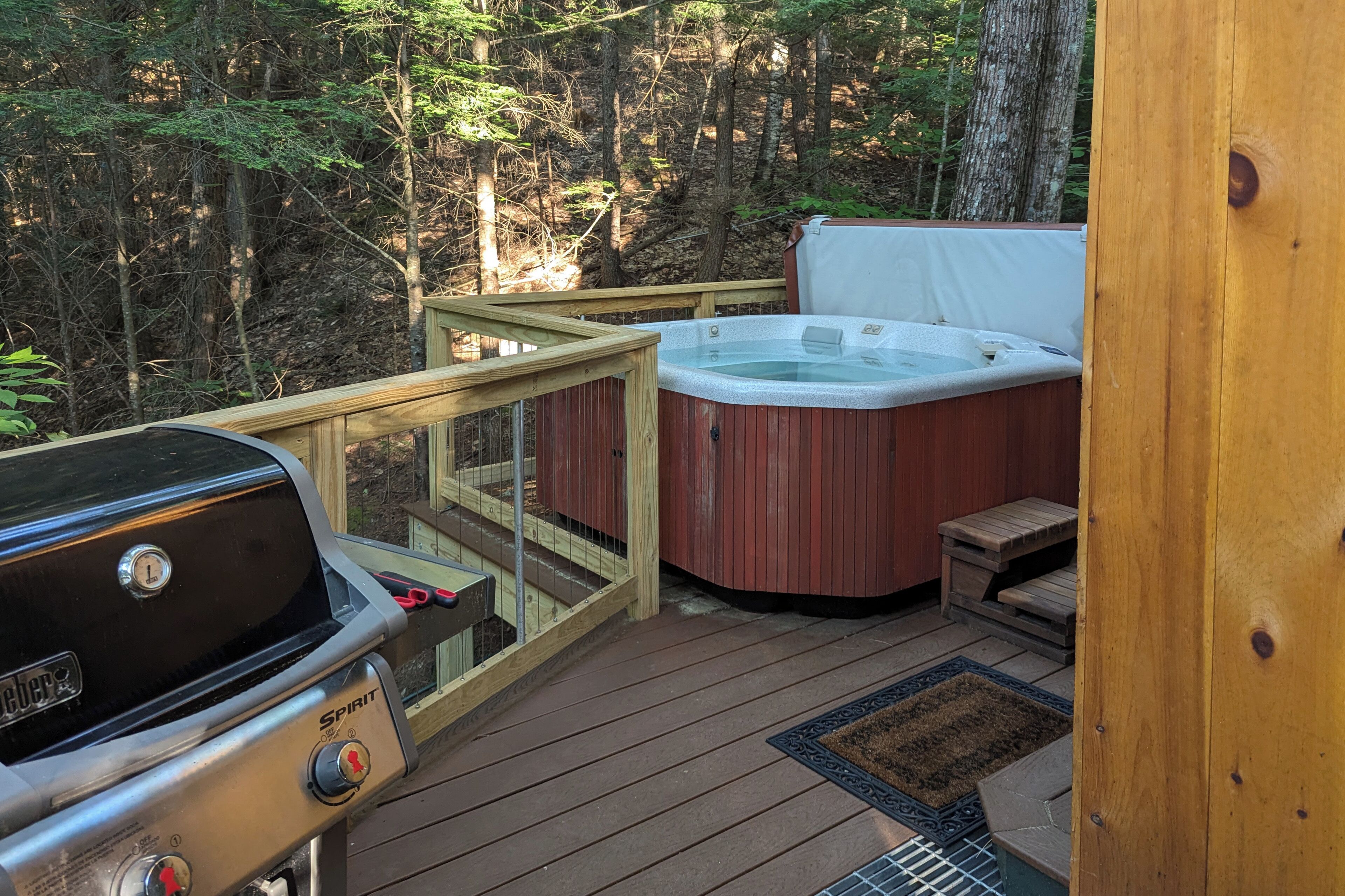 Una terraza con jacuzzi, parrilla y barandilla de madera.