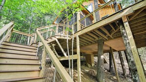 A wooden deck with a staircase leading to a wooden cabin surrounded by trees. - Tree House w/ Hot Tub: Near Sunday River Resort! (Rumford)