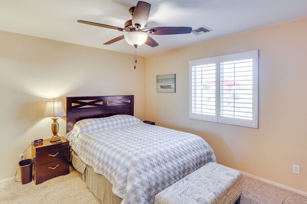 A bedroom with a bed, a nightstand, a lamp, a ceiling fan, a window with blinds, and a wall-mounted picture. - 5 Mi to CO River: Home w/ Pool in Fort Mohave! (Fort Mohave)