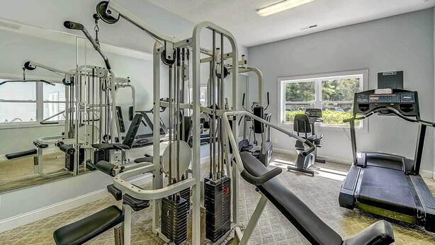 Un gimnasio con diversos equipos de ejercicio, una cinta de correr y un espejo grande.