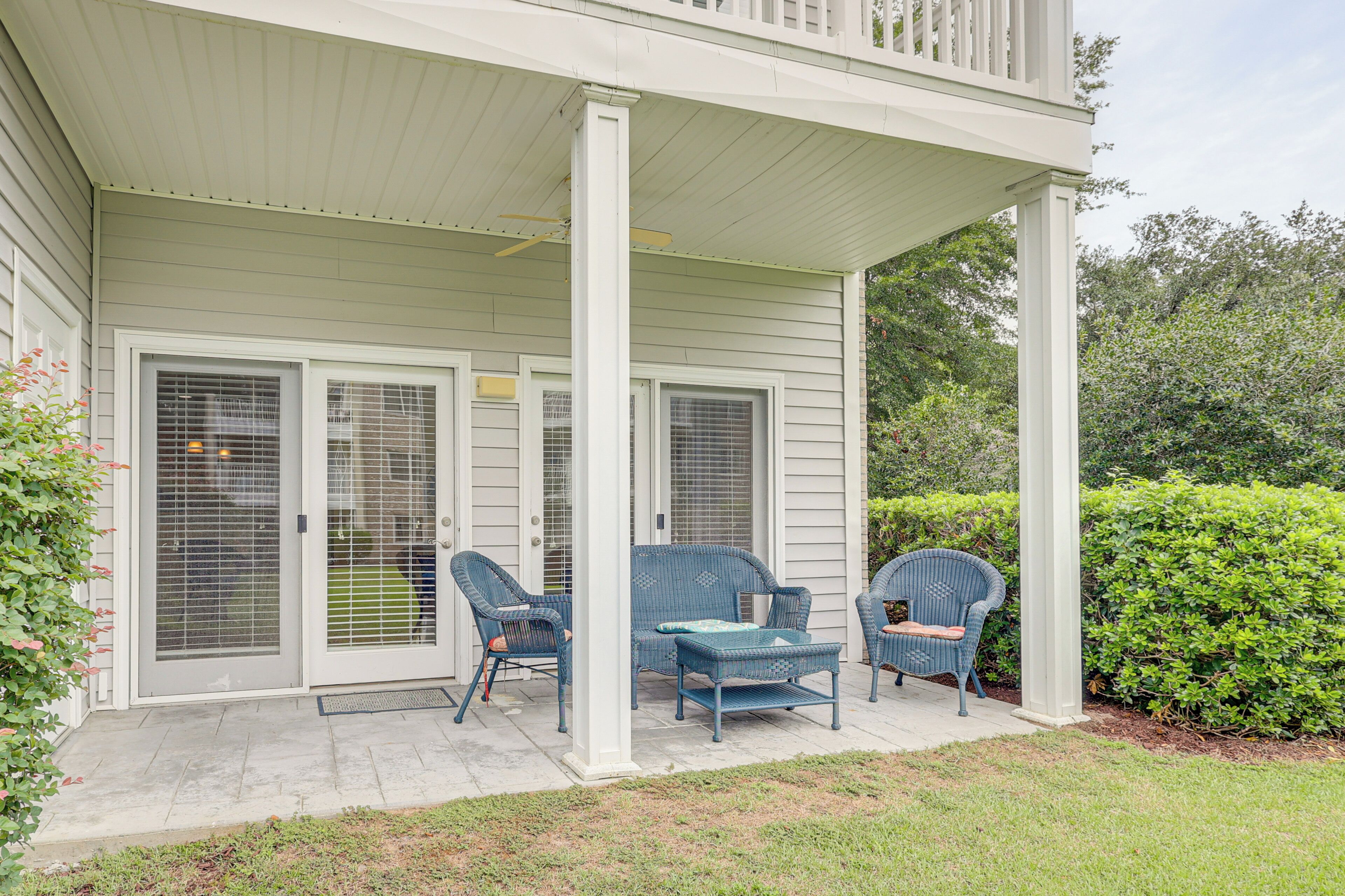 A covered porch with two chairs and a bench, a white railing, and a door with a window.