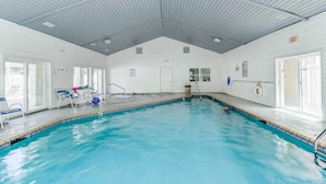 Una piscina interior con carriles delimitados, una silla de socorrista y un área de piscina con sillas y una mesa.