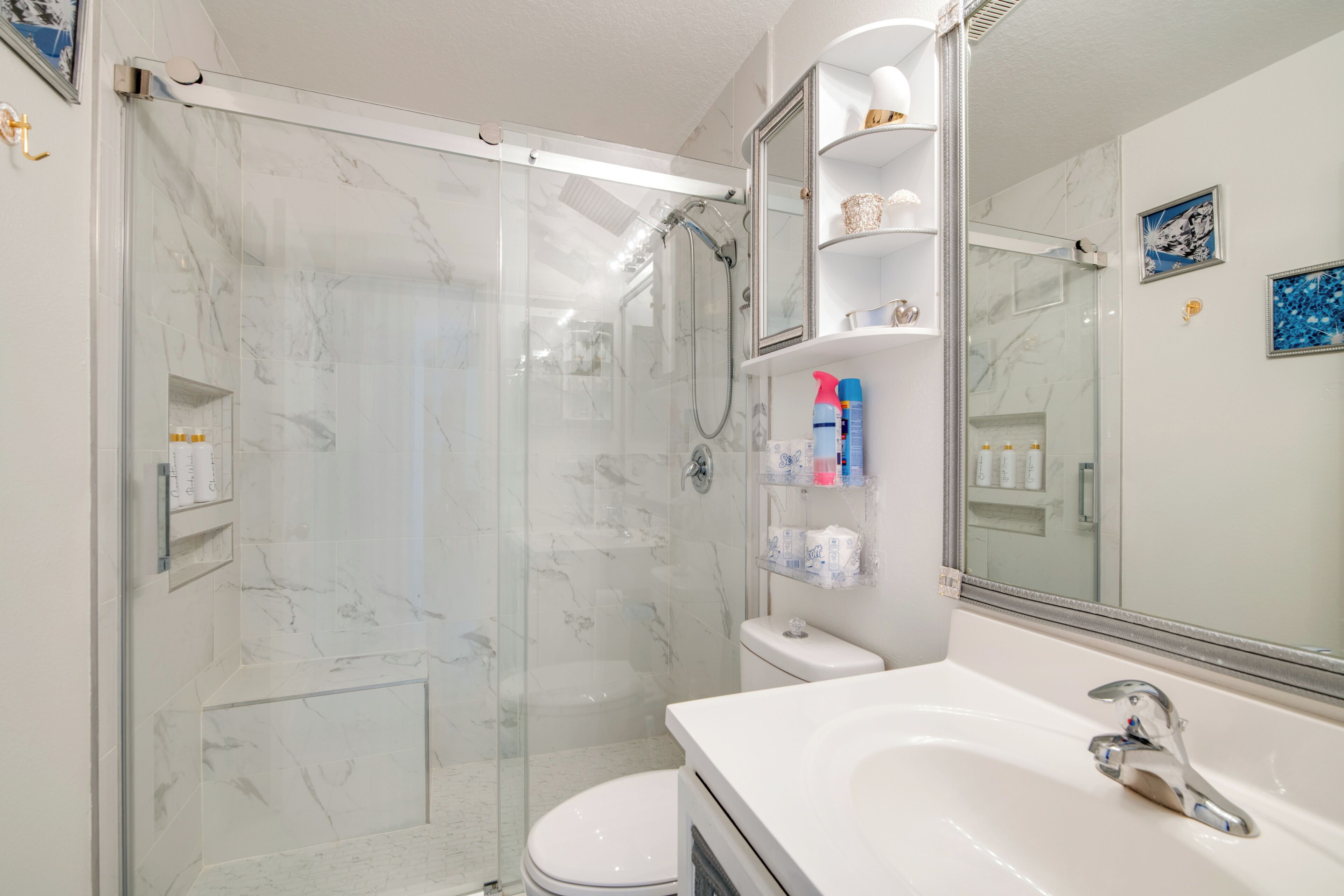 A modern bathroom with a glass-enclosed shower, a white toilet, and a vanity with a large mirror.